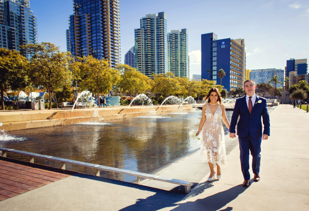 Wedding couple hold hands after getting married at the San Diego Courthouse with the downtown waterfront park in the background 